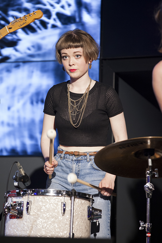 A musician playing drums in front of projected visuals.