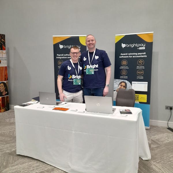 Two Bright employees standing in front of signs promoting BrightPay at a conference