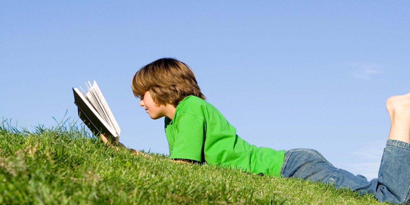 Boy laying on grass studying 