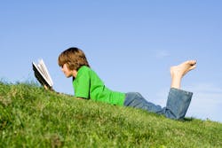 Boy laying reading on grass