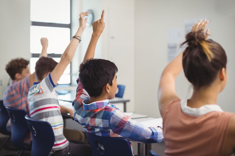 students in a class with hands up 