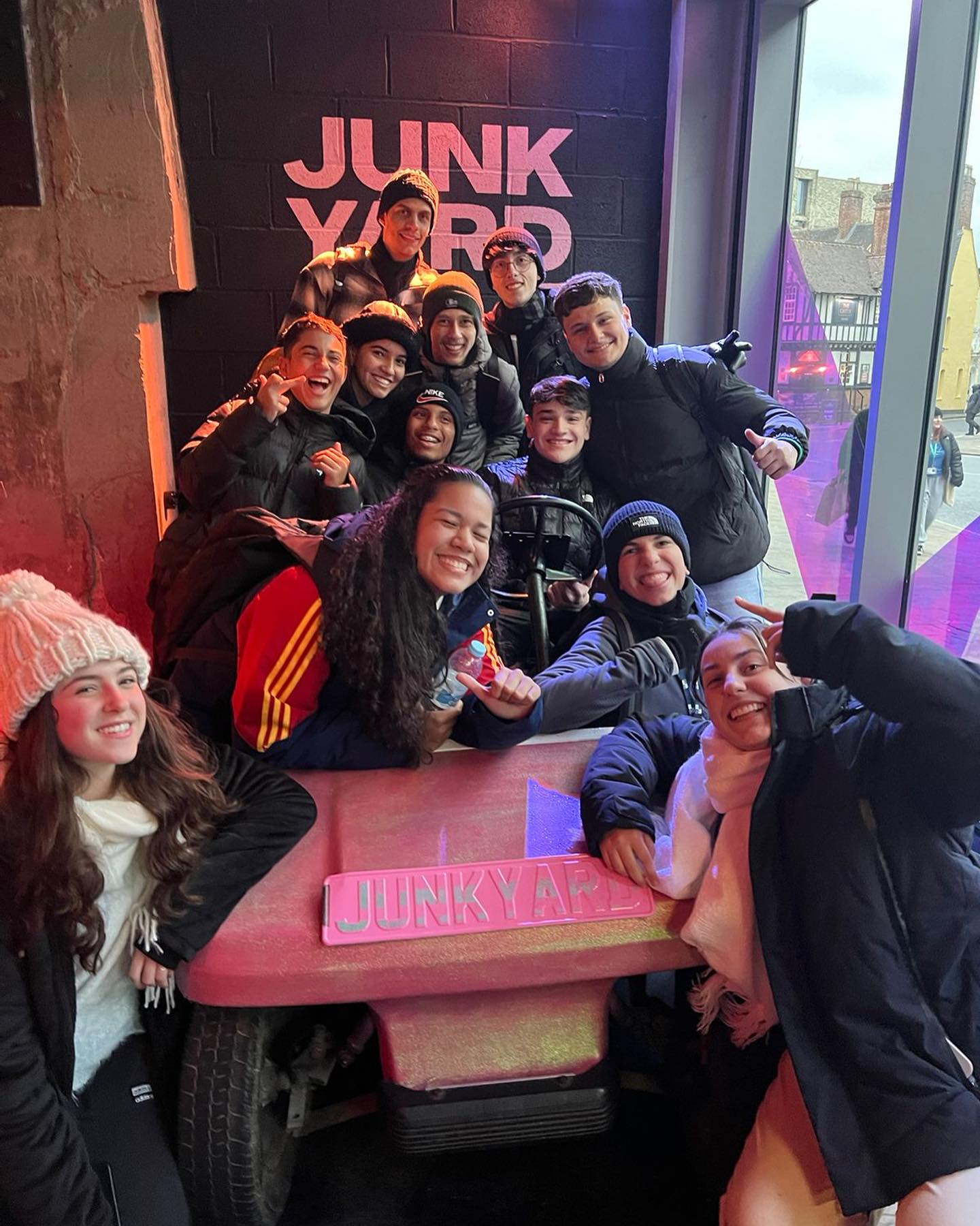 A group of students crowded around a model go-kart. The wall behind them has been painted with the text "JUNK YARD". 
