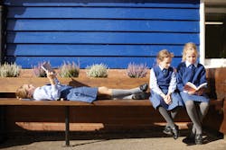 Three Aysgarth students reading on a bench. One student is laying down to read, whilst the other two sit upright.