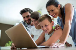 A young boy is on a laptop whilst his family watch over his shoulder