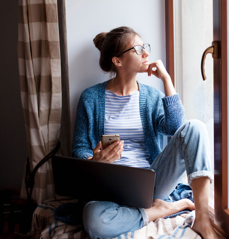 girl sitting with a laptop looking out the window 