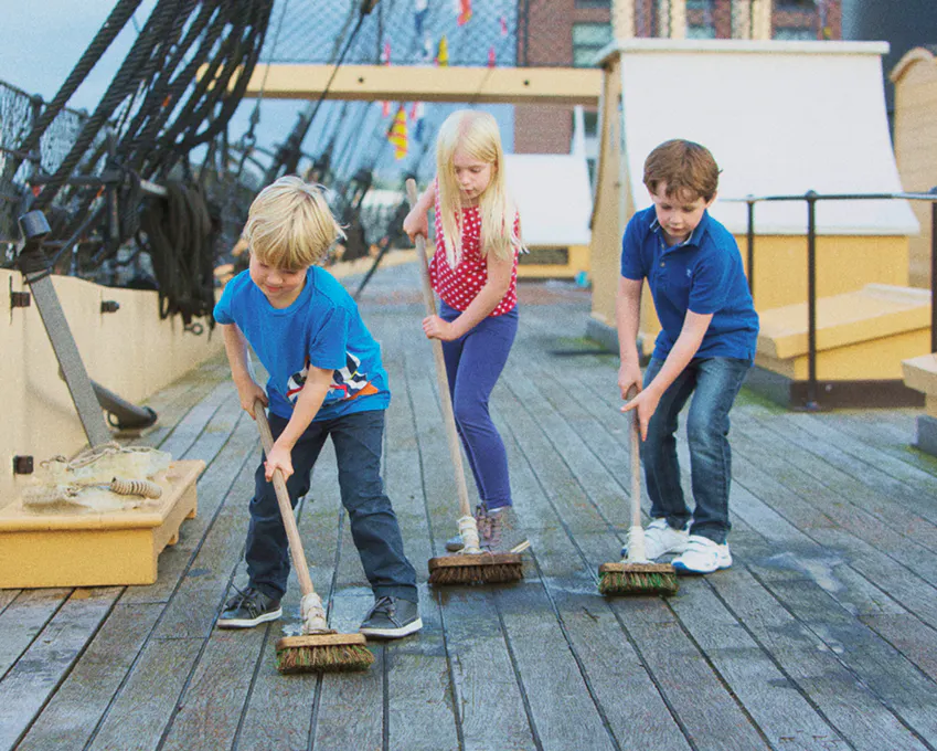 3 children "scrubbing" the deck on-board the ship