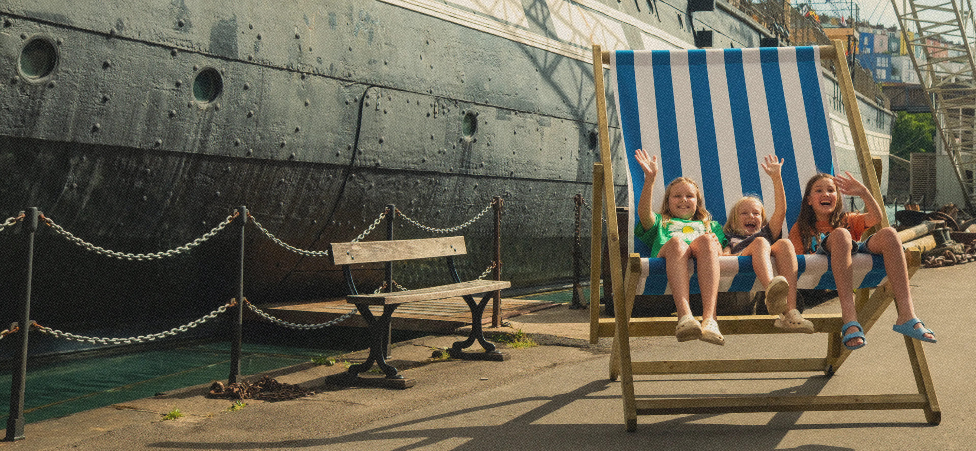 Three children on a big deck chair in front of the SS Great Britain at Bristol Dockyards