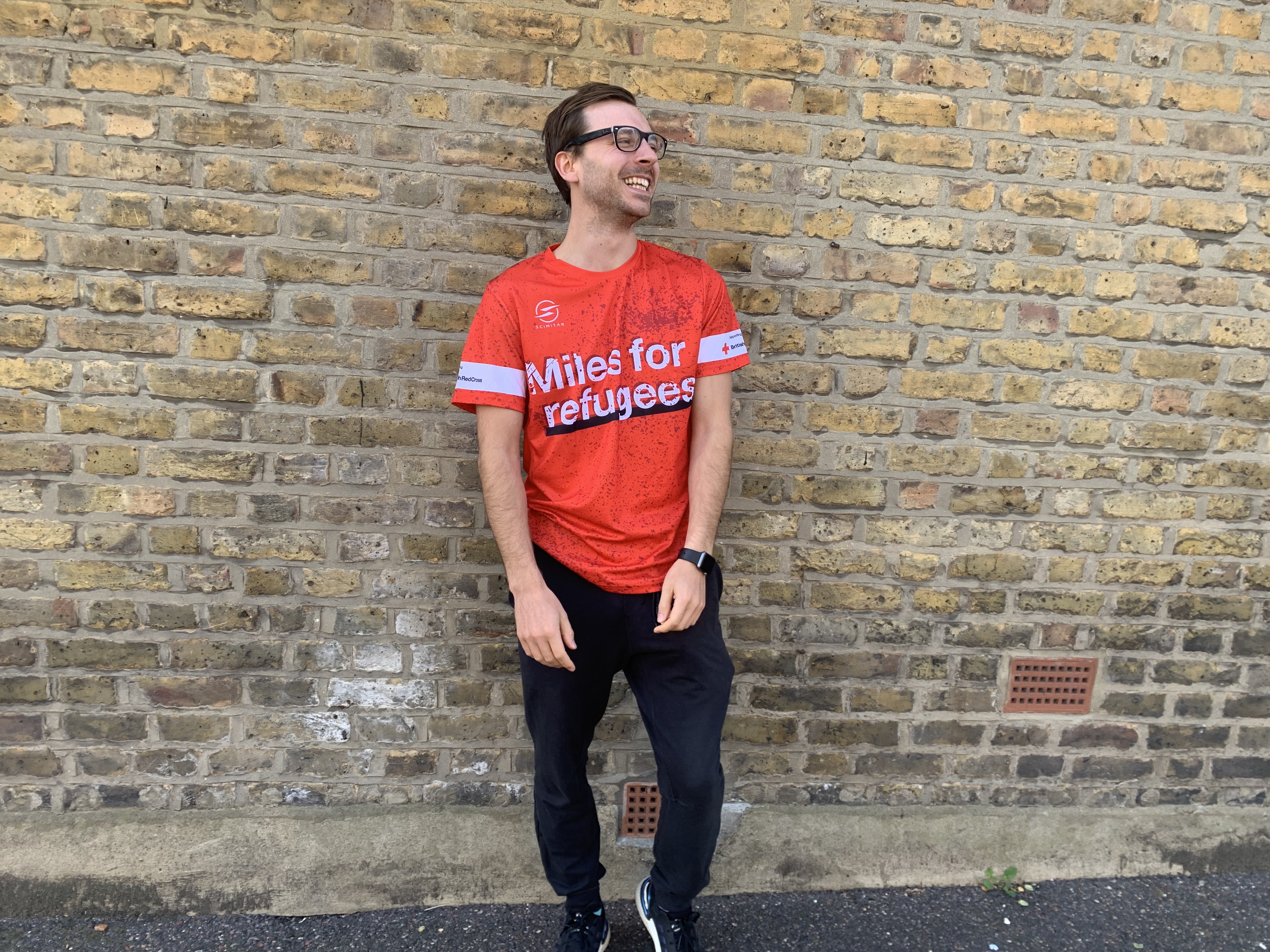 Image of man against a brick wall wearing a red Miles for Refugees t-shirt