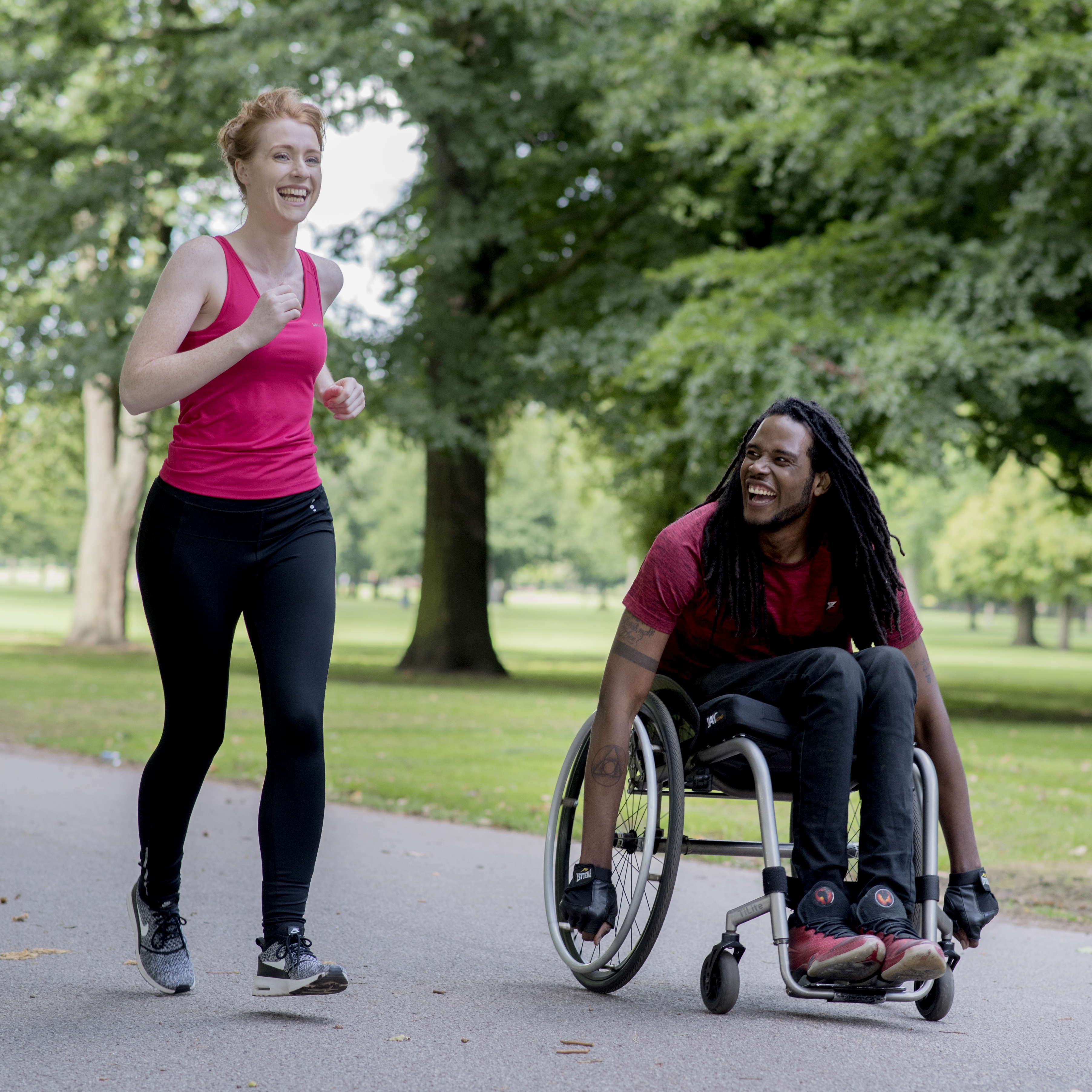 Man in a wheelchair next to a woman running, both smiling together