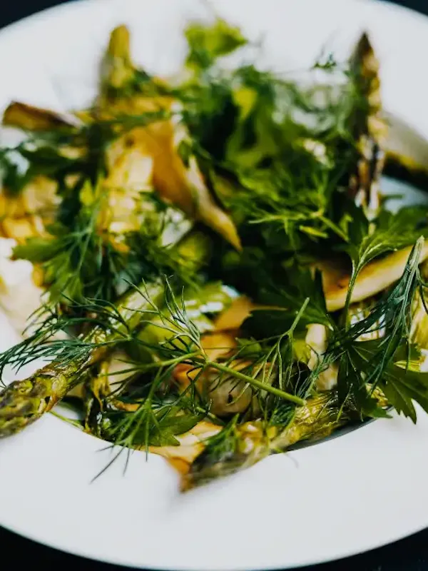 Wit diep bord met geroosterde groene asperges, kaas Fransje van Mathilde en verse kruiden