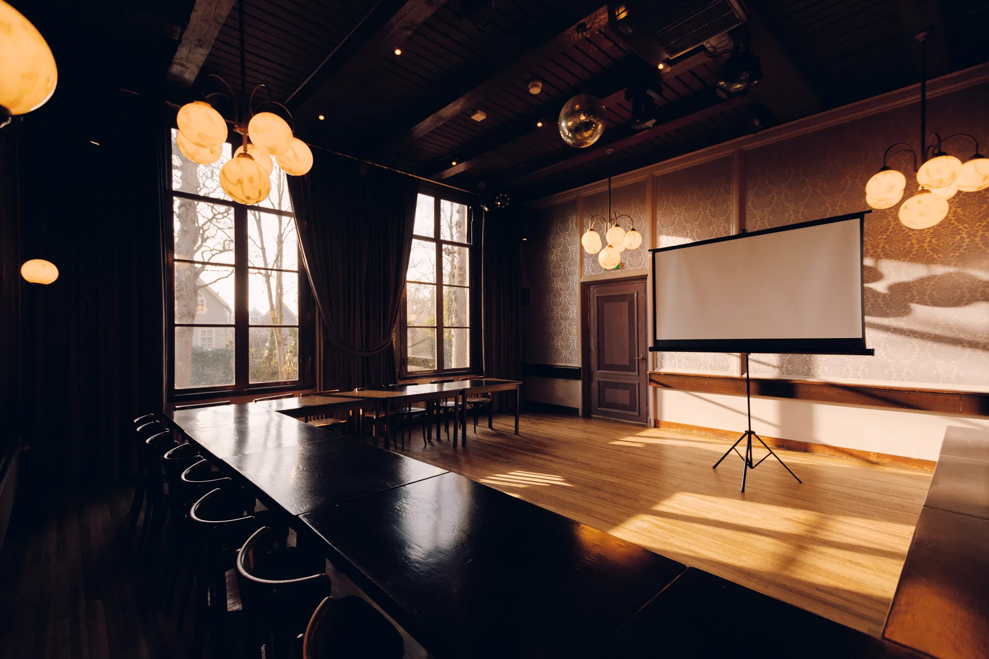 De Grote Zaal ingericht om te vergaderen, met een lange tafel en een projectiescherm