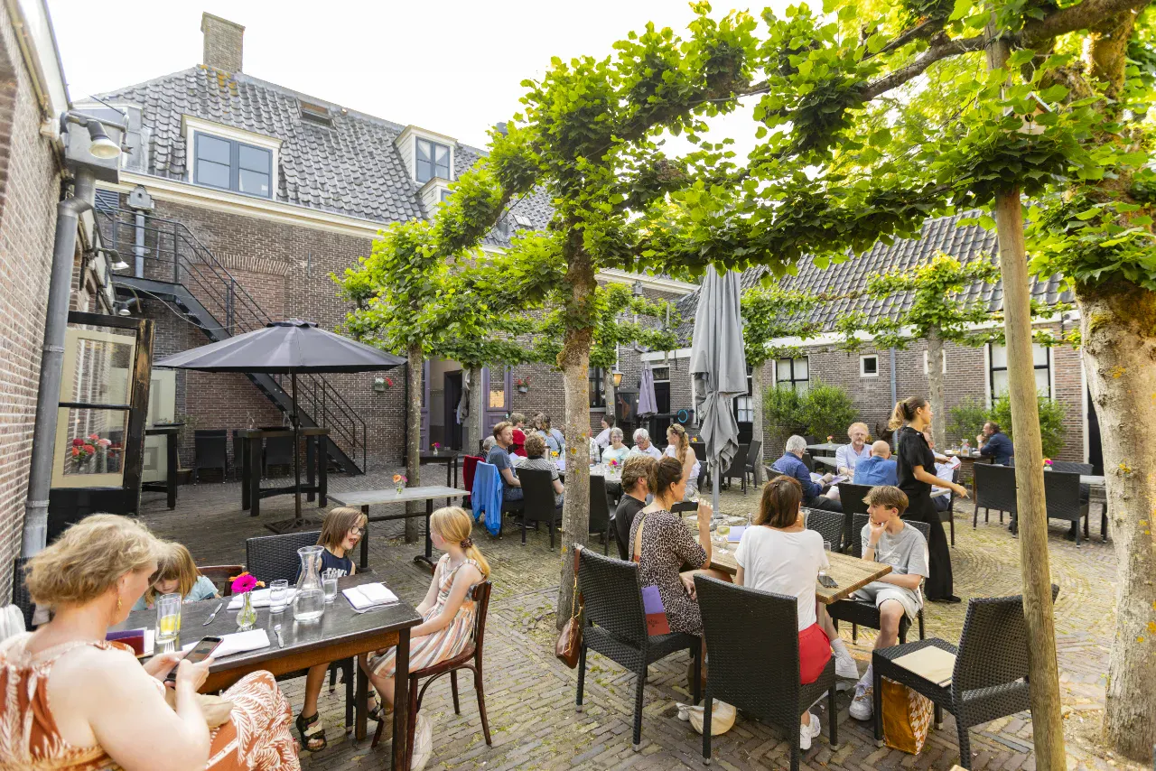 Gasten aan de koffie en lunch op de binnenplaats van Het Broeker Huis, onder de bomen