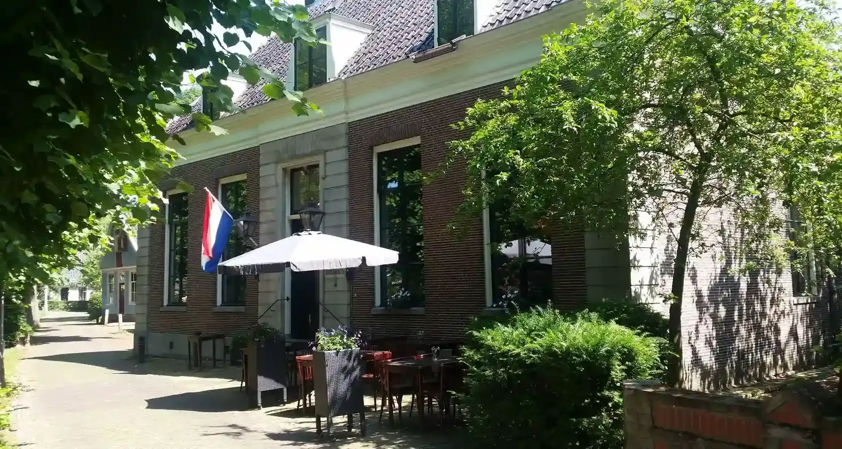 Het Broeker Huis exterieur terras zomer breed parasol en Nederlandse vlag