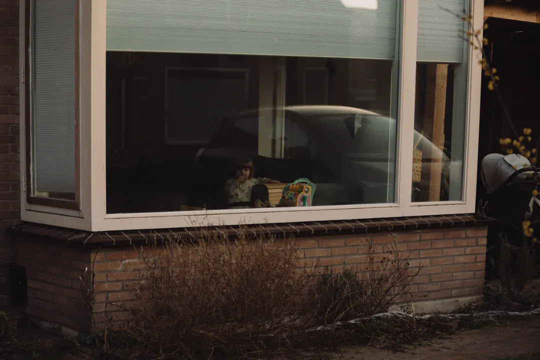 Peuter achter raam met speelgoed en auto reflectie