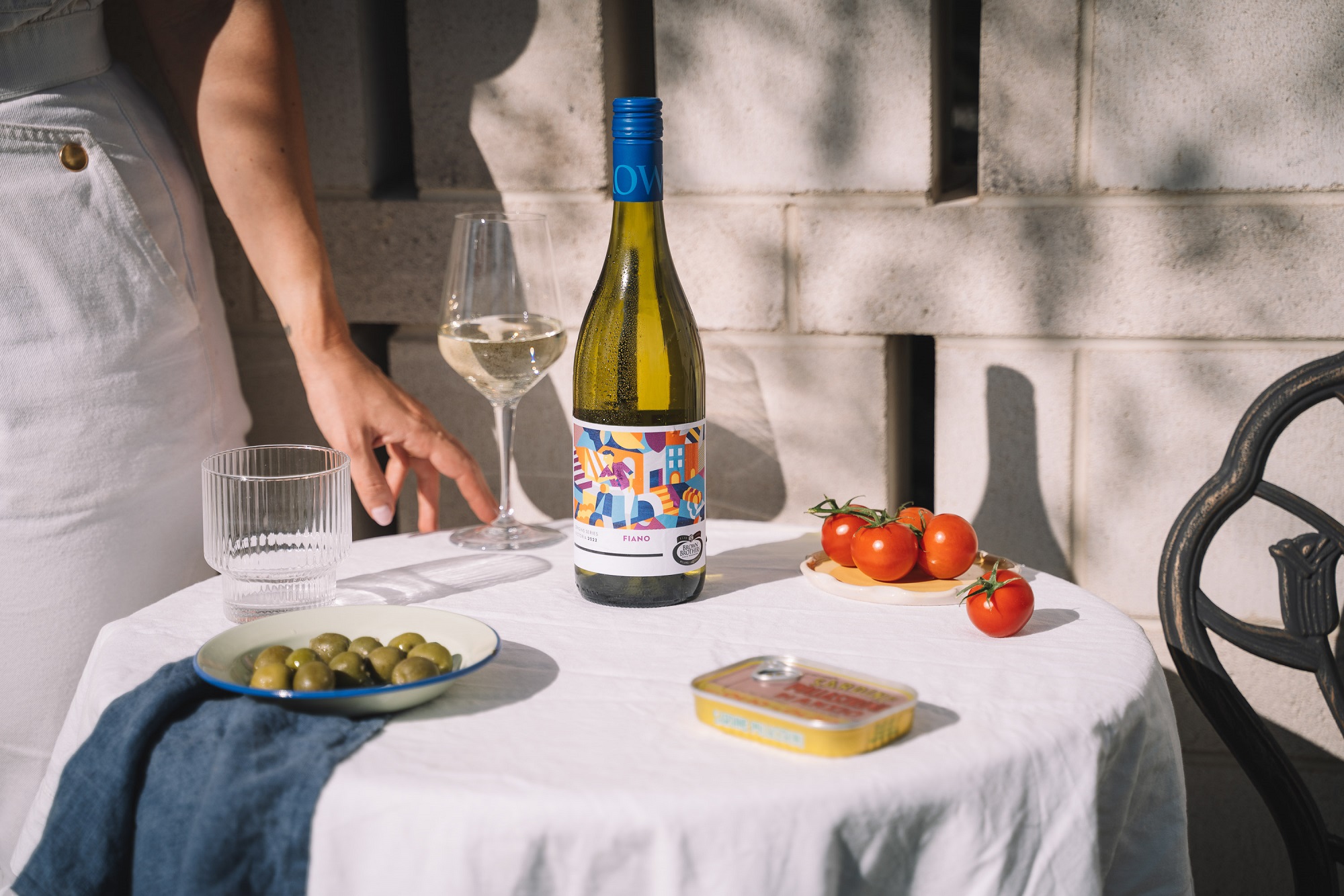 bottle of Origins Series Fiano on an outdoor table set with olives, tomatoes, wine glass