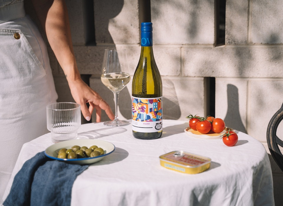 bottle of Origins Series Fiano on an outdoor table set with olives, tomatoes, wine glass