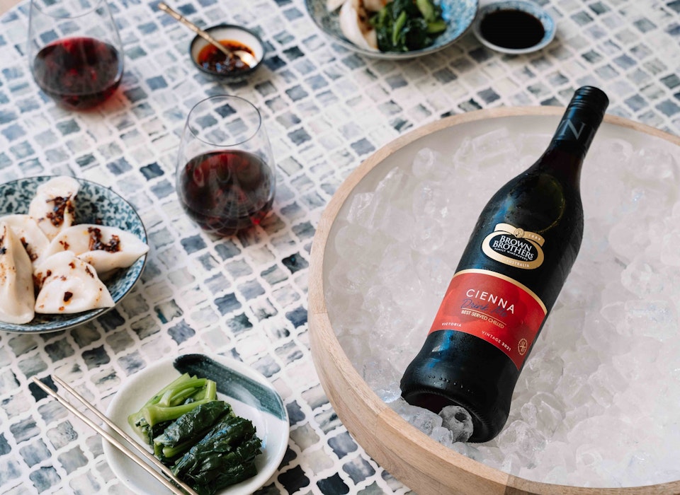 bottle of cienna lying flat in an ice bucket atop a blue tiled table served with asian greens and dumplings