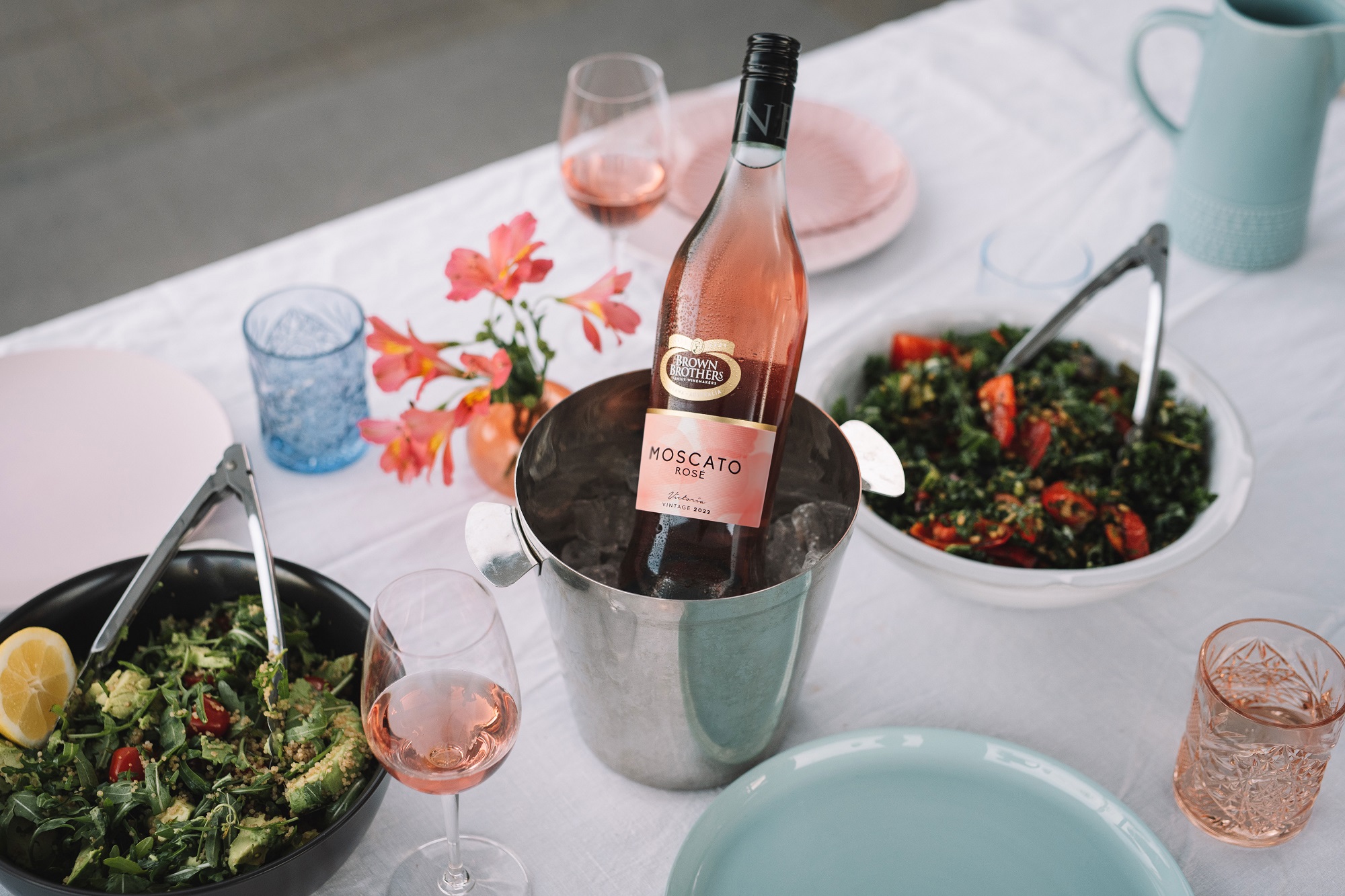 bottle of Moscato Rose in an ice bucket in the middle of a table set with food and wares