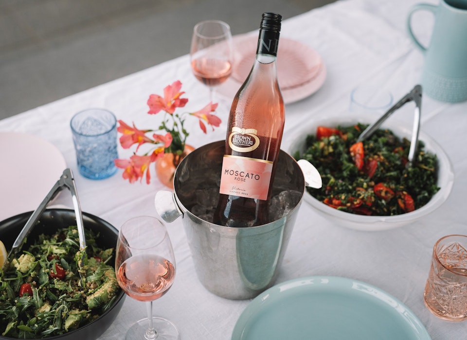 bottle of Moscato Rose in an ice bucket in the middle of a table set with food and wares