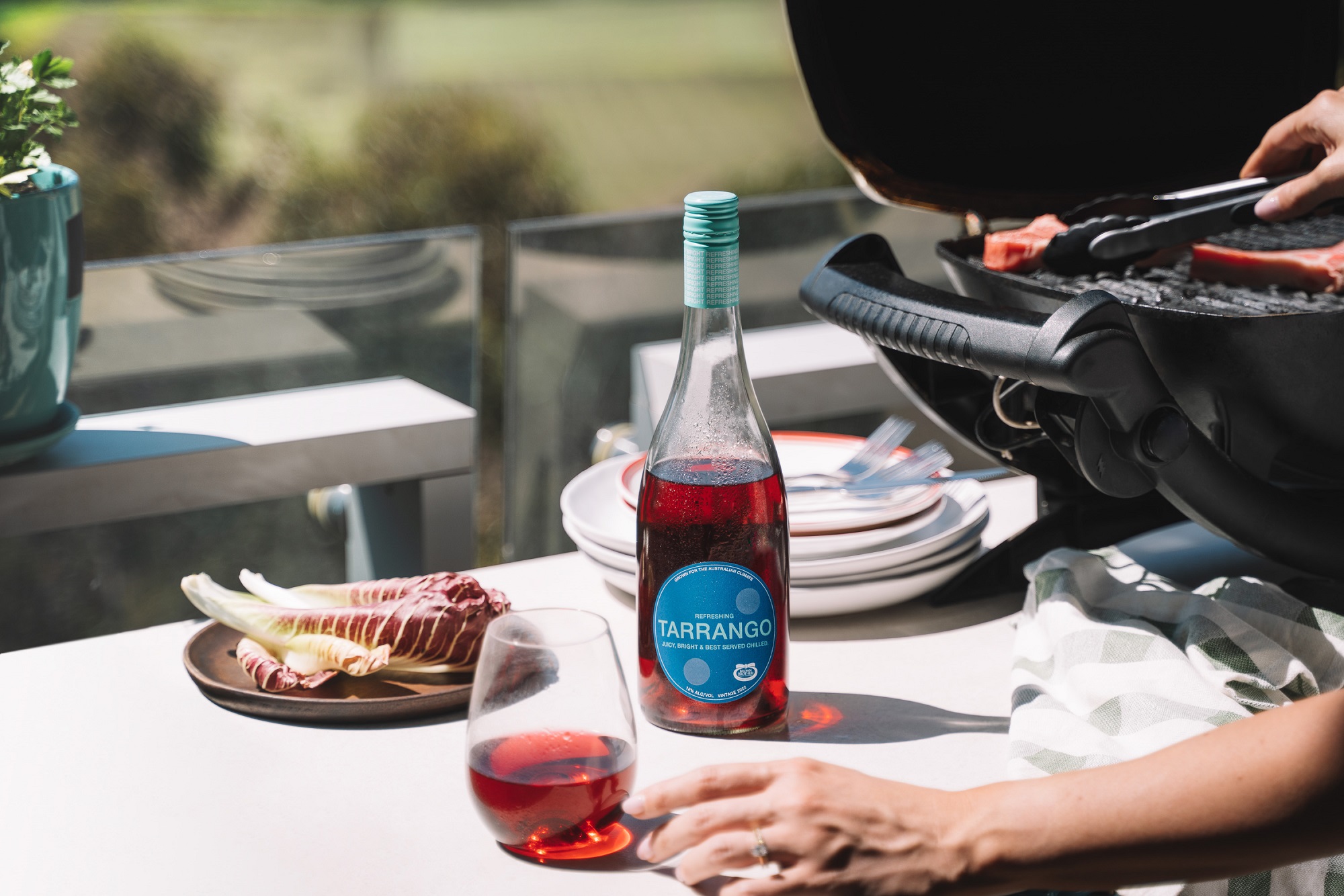 A glass and bottle of Tarrango, sitting on an outdoor table next to a BBQ overlooking a park