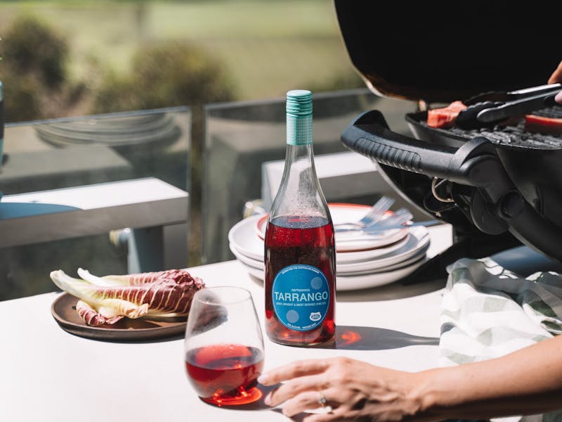 A glass and bottle of Tarrango, sitting on an outdoor table next to a BBQ overlooking a park