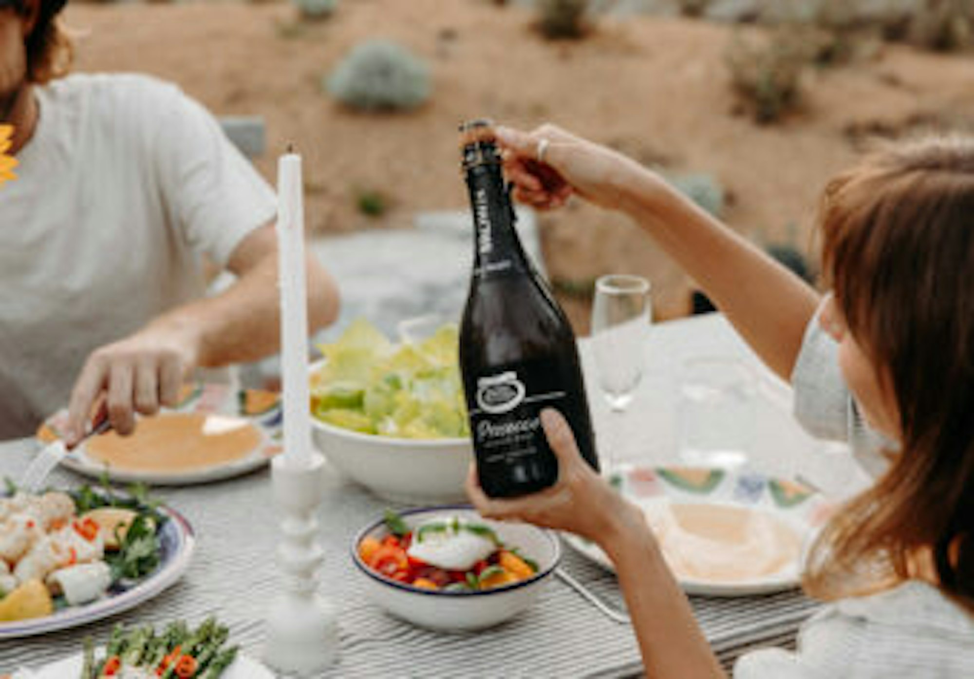 Bottle of Brown Brothers Premium Prosecco Brut in hand over a summer spread