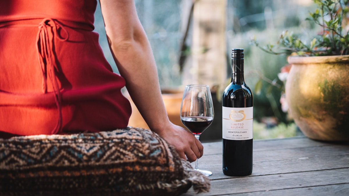 Person sitting on cushin holding glass of red wine 