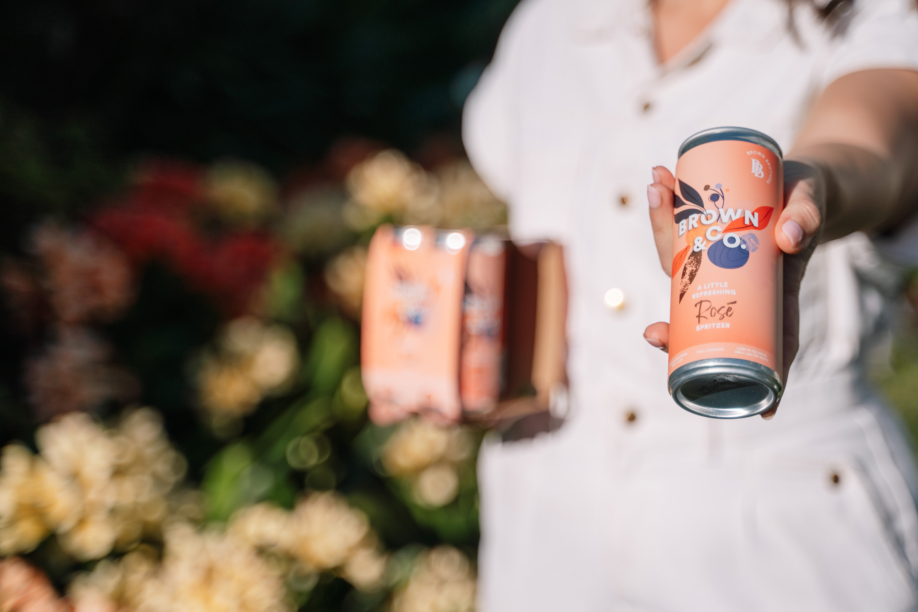 girl holding out a 4 pack with a can of brown & co rose 