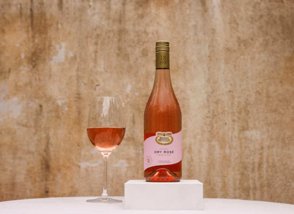 A bottle of Brown Brothers Classic Dry Rose with a glass of wine with rose in it.