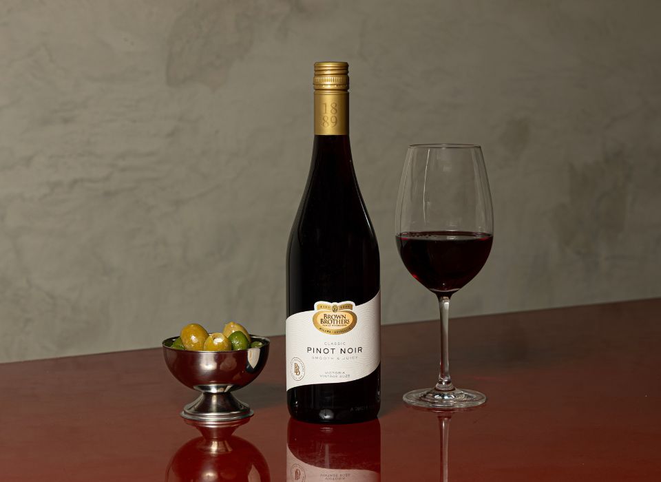 A bottle of Brown Brothers Pinot Noir, a glass of wine and some olives