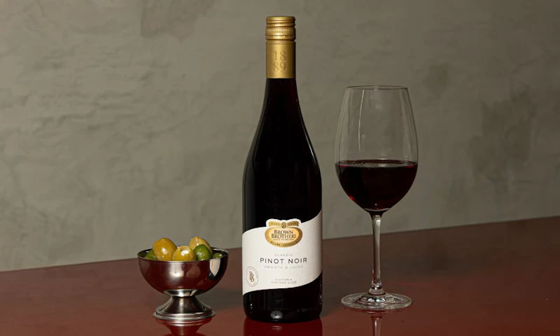 A bottle of Brown Brothers Pinot Noir, a glass of wine and some olives