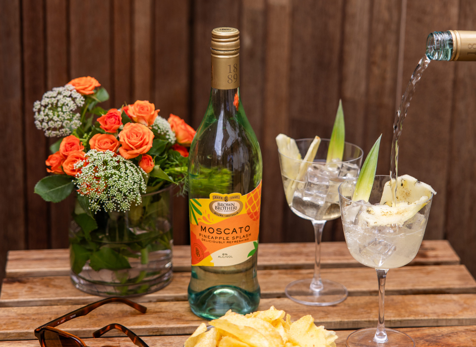 A bottle of Brown Brothers Pineapple Splash Moscato with 2 glasses.
