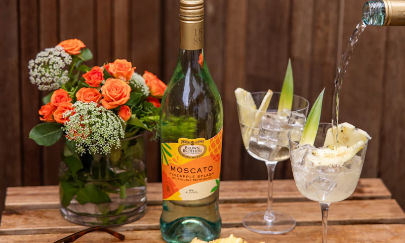 A bottle of Brown Brothers Pineapple Splash Moscato with 2 glasses.