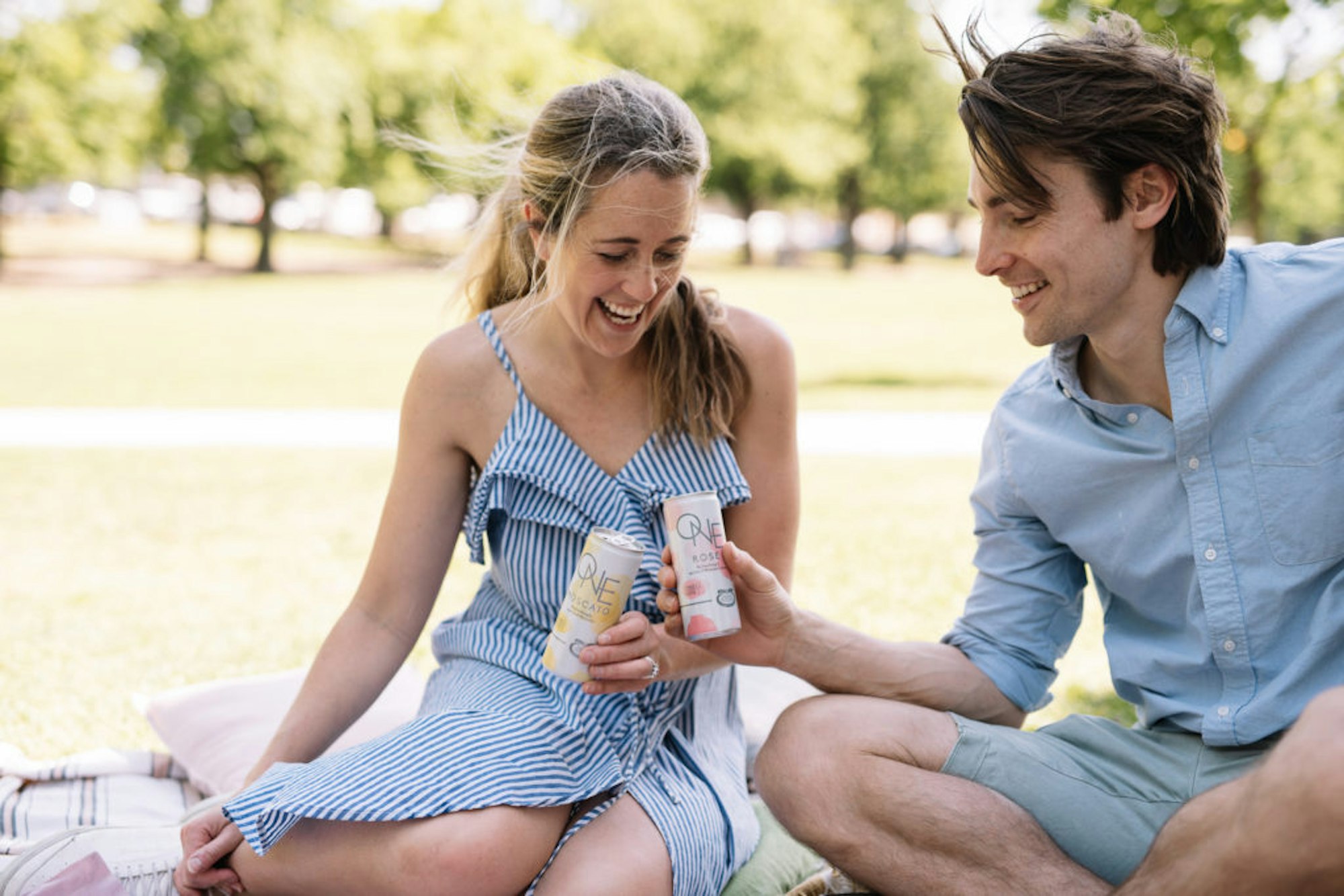 Man and women holding Moscato One Cans sitting on a picnic rug