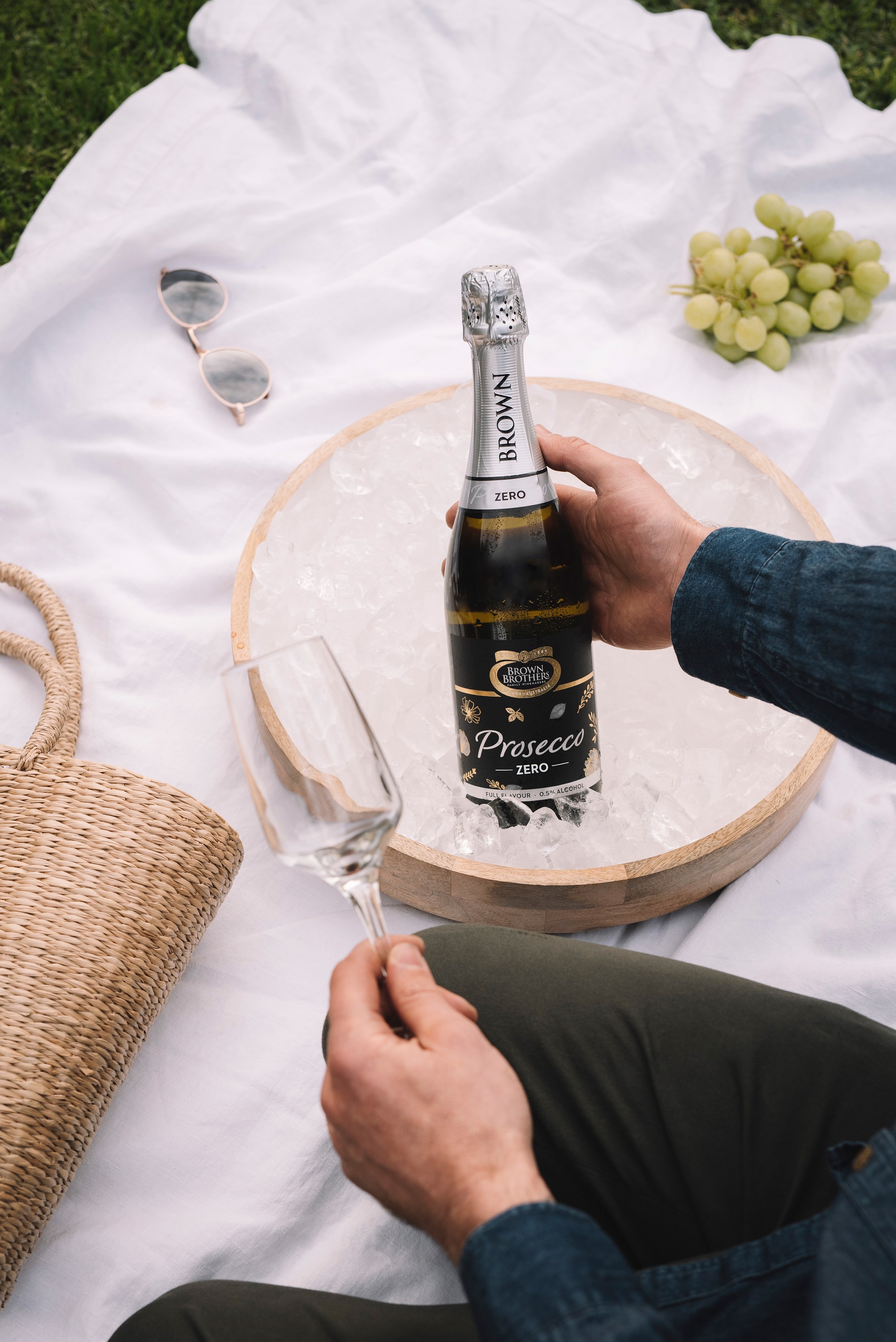 bottle of prosecco zero being picked up from a flat ice bucket atop a white picnic blanket