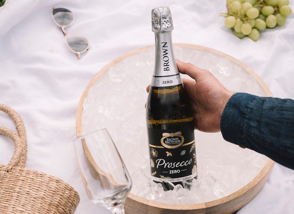 bottle of prosecco zero being picked up from a flat ice bucket atop a white picnic blanket