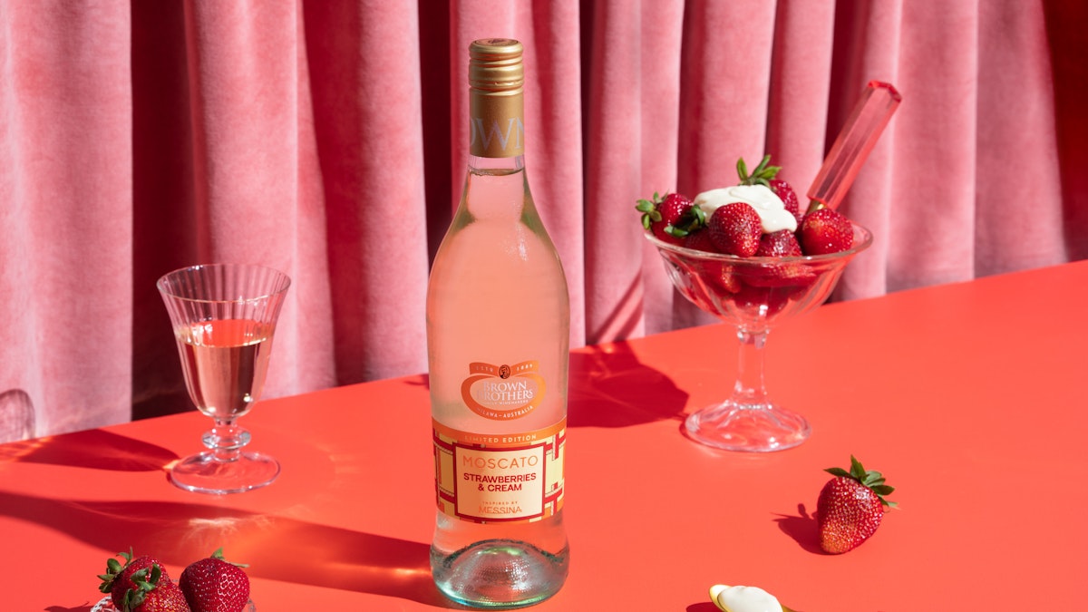 Bottle of Brown Brothers Limited Edition Moscato Strawberries & Cream next to a bowl of ice cream and strawberries