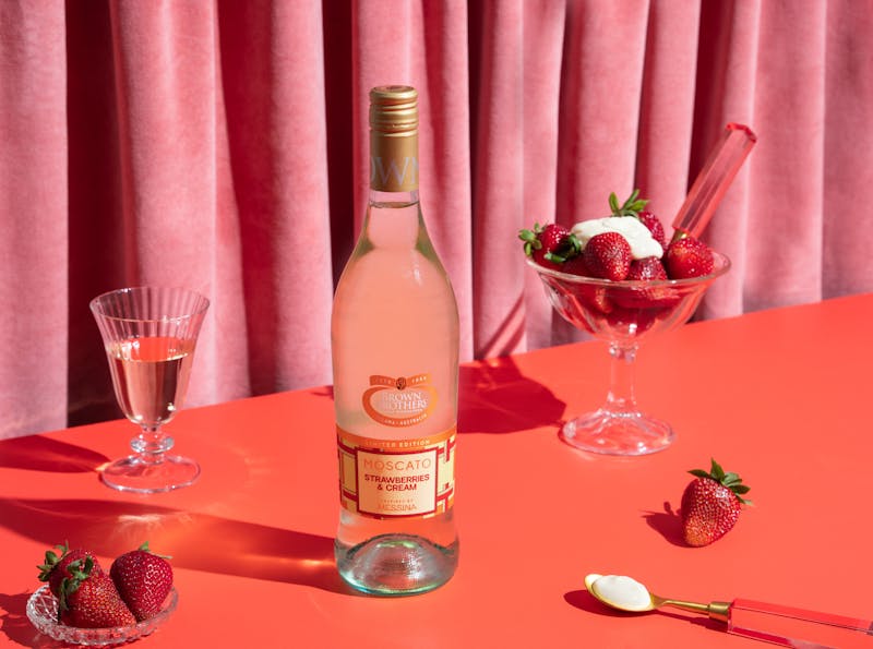 Bottle of Brown Brothers Limited Edition Moscato Strawberries & Cream next to a bowl of ice cream and strawberries