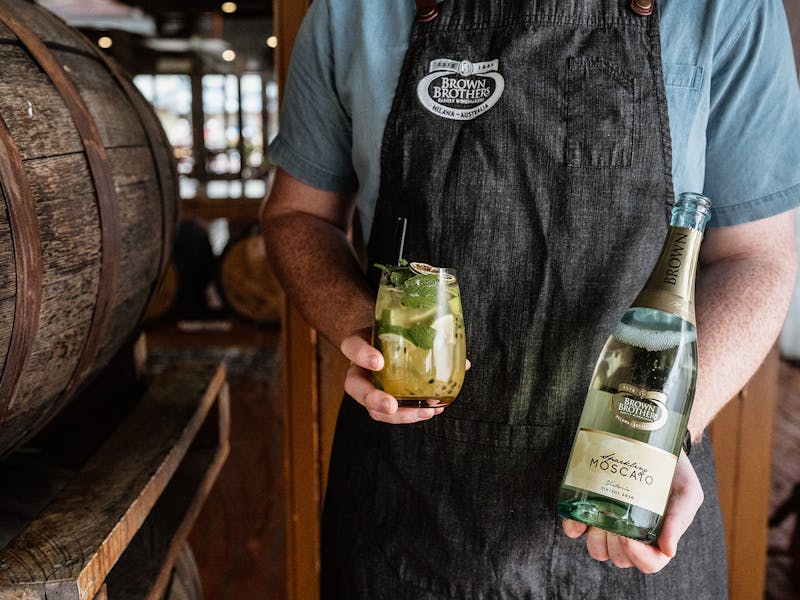 Brown Brothers team member holding a bottle of sparkling moscato and a cocktail