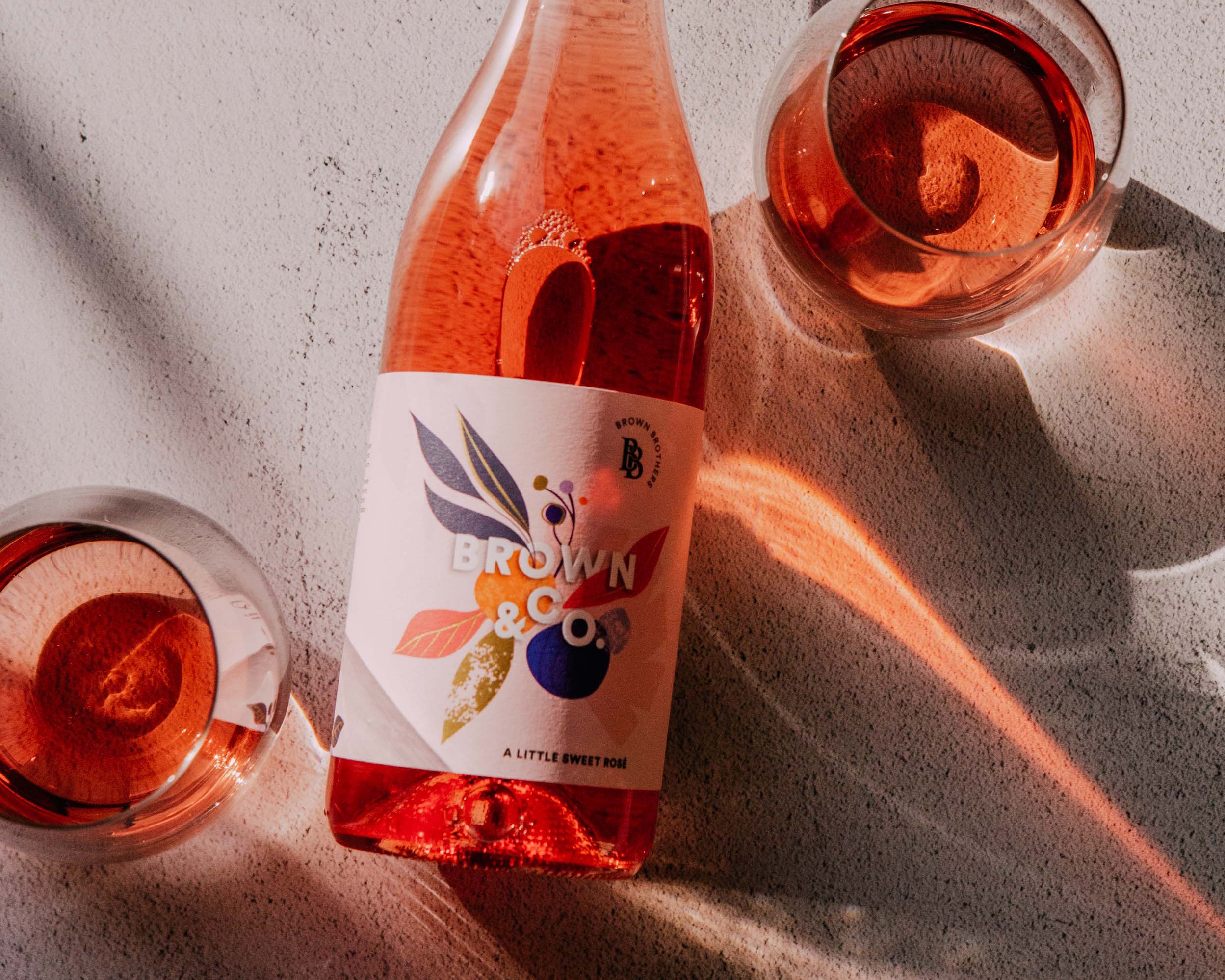 bottle of brown & co rose with two glasses in hard lighting 