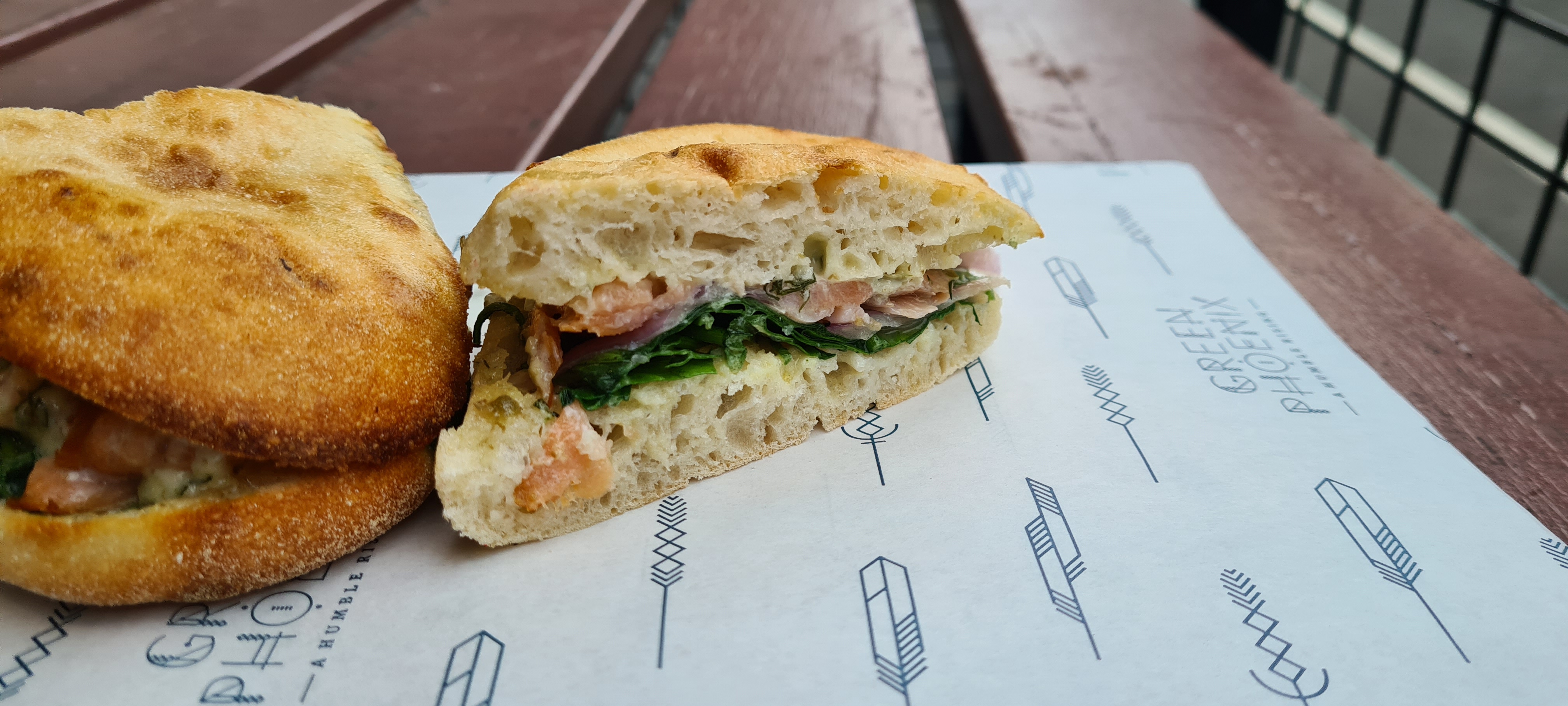 Salmon and spinach in a focaccia, sitting on top of branded paper packaging