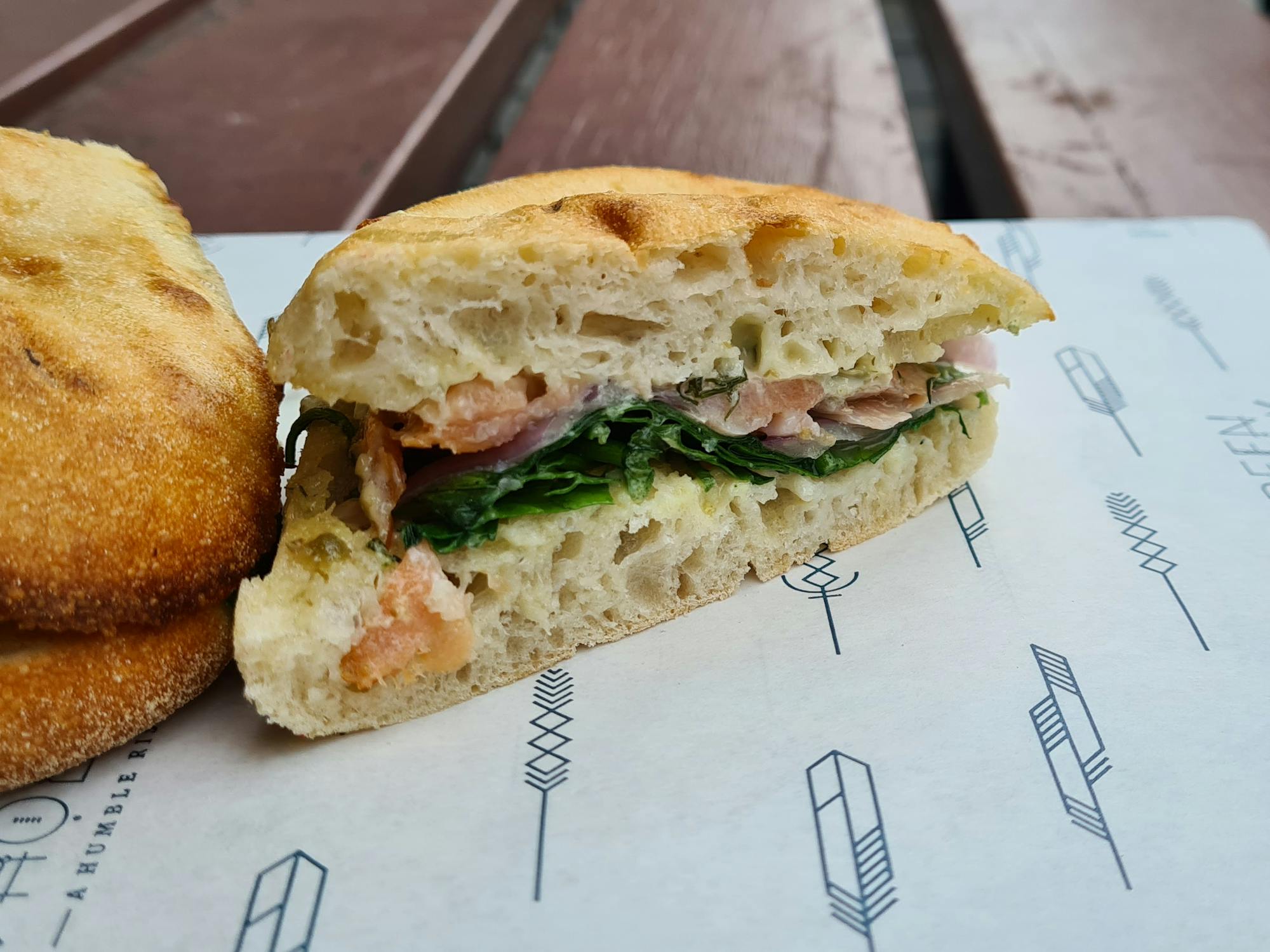 Salmon and spinach in a focaccia, sitting on top of branded paper packaging