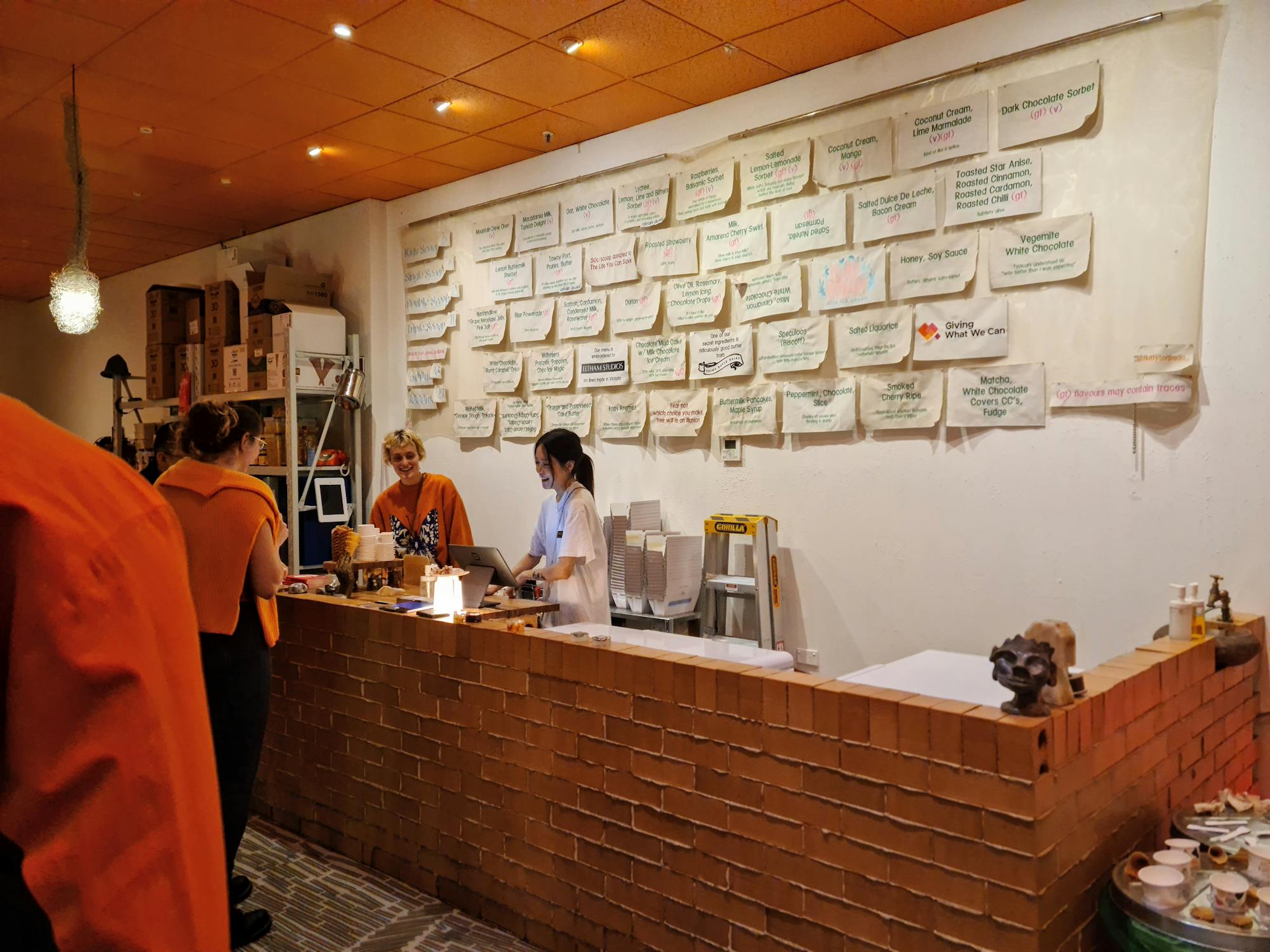 Two servers behind a brick counter serving gelato from eskies.