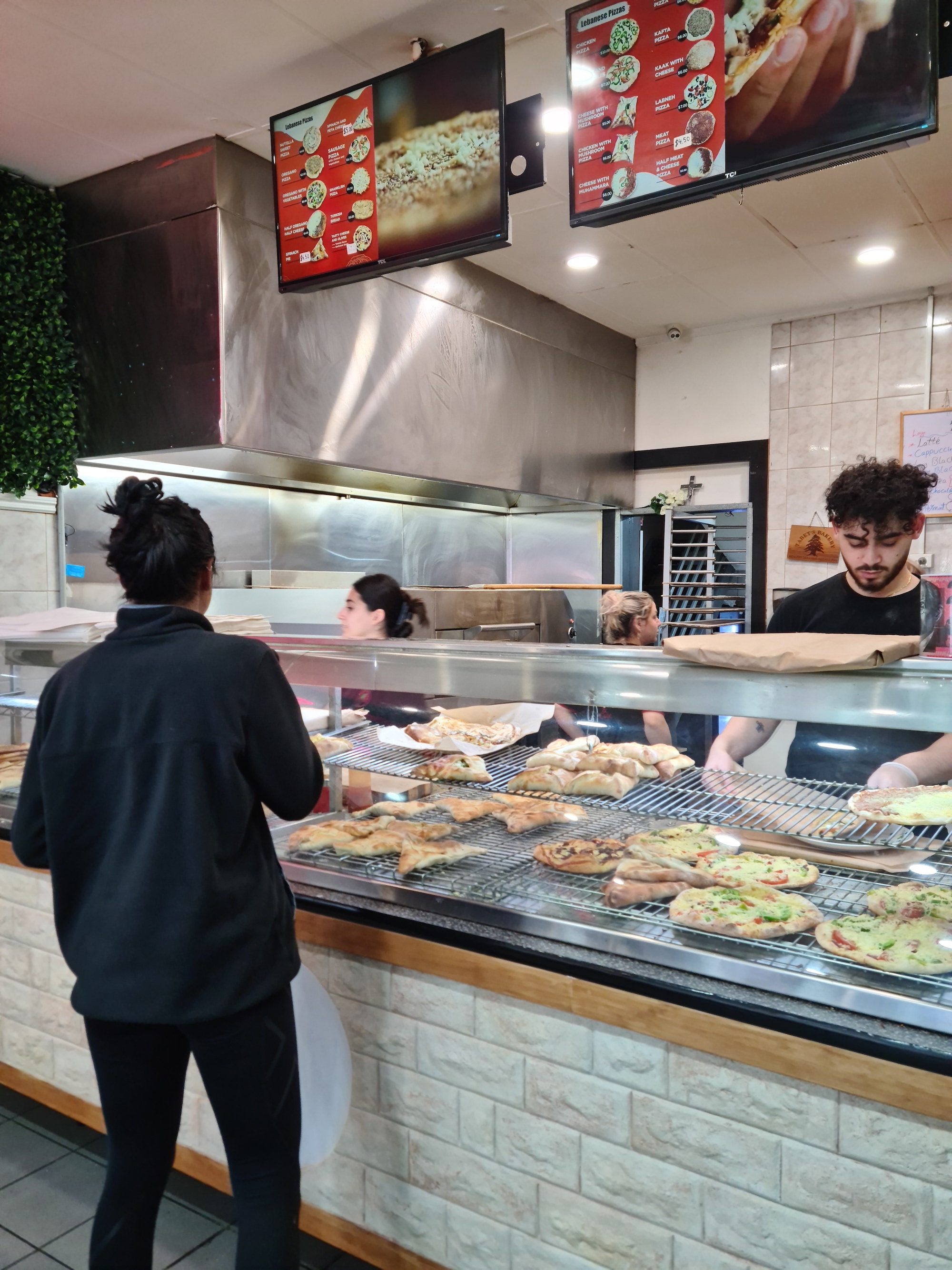 A woman looking at a glass case of many pre-prepared pizzas and pockets