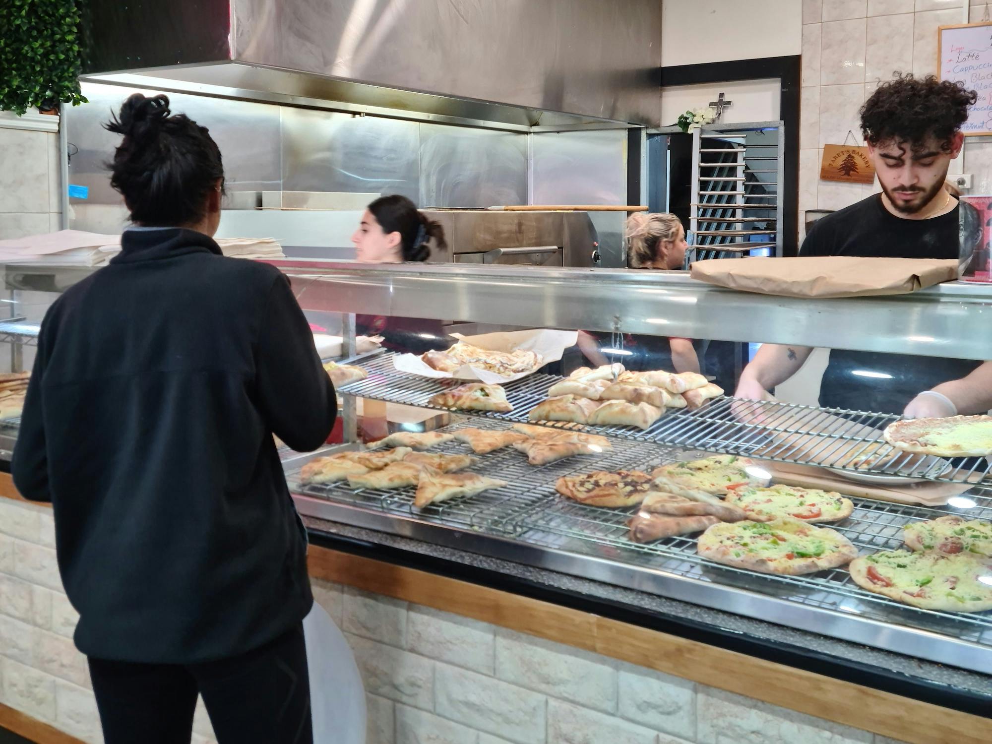 A woman looking at a glass case of many pre-prepared pizzas and pockets