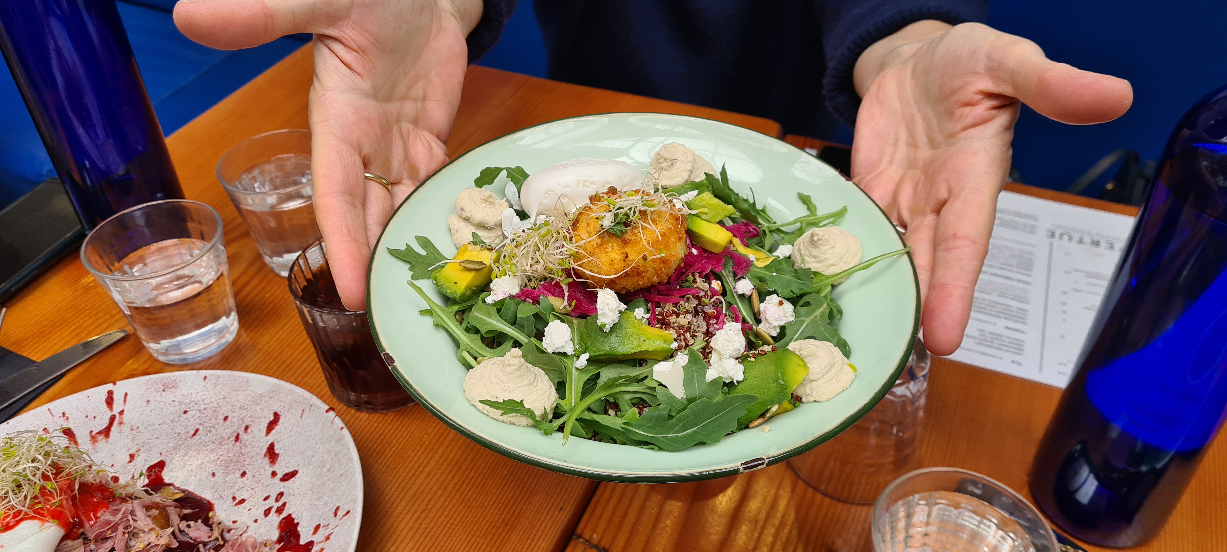A salad bowl with pieces of cheese and a fried arancini ball on a bed of rocket. 