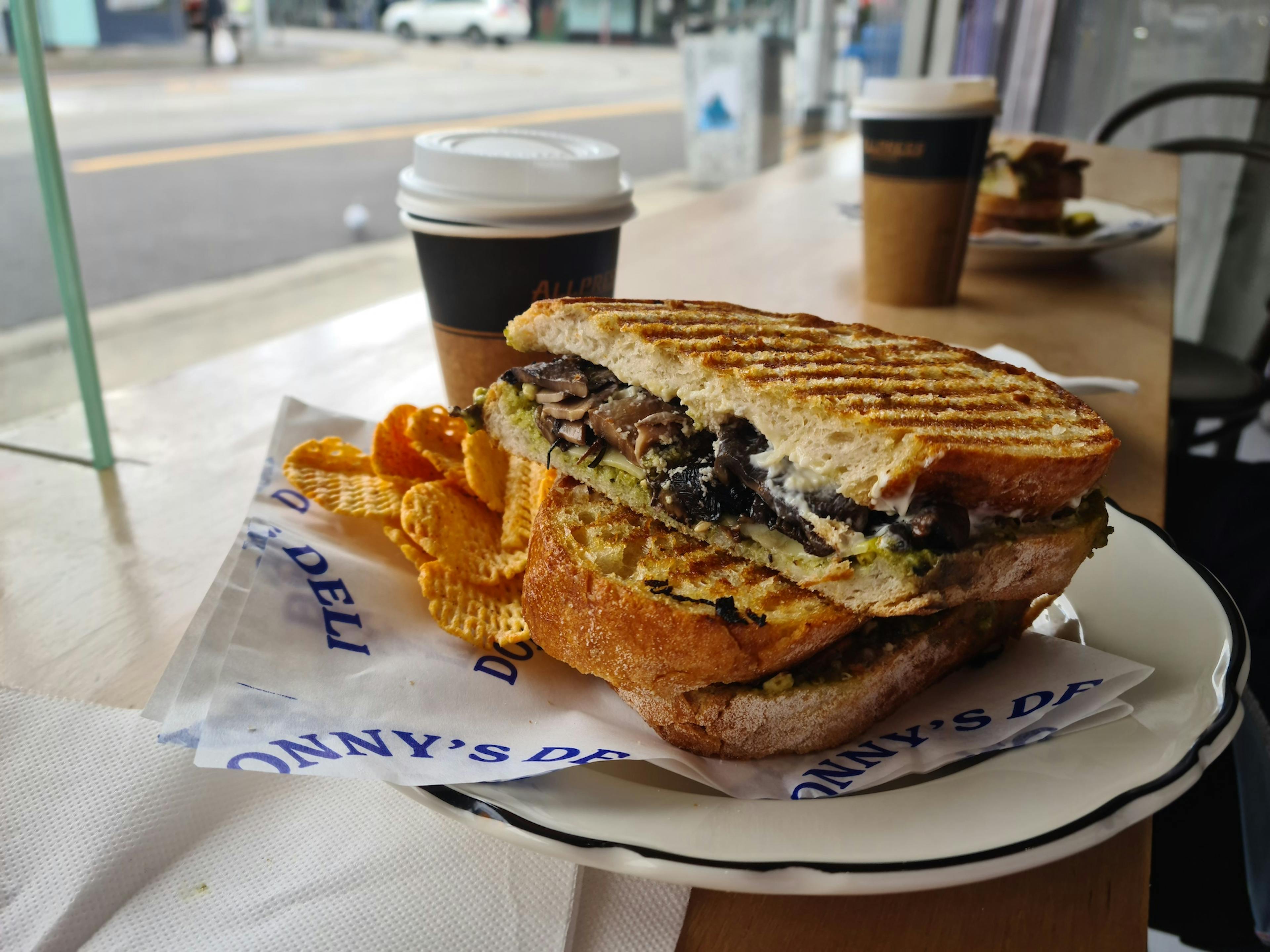 Mushroom toastie served with crisps and a long black coffee in the background.