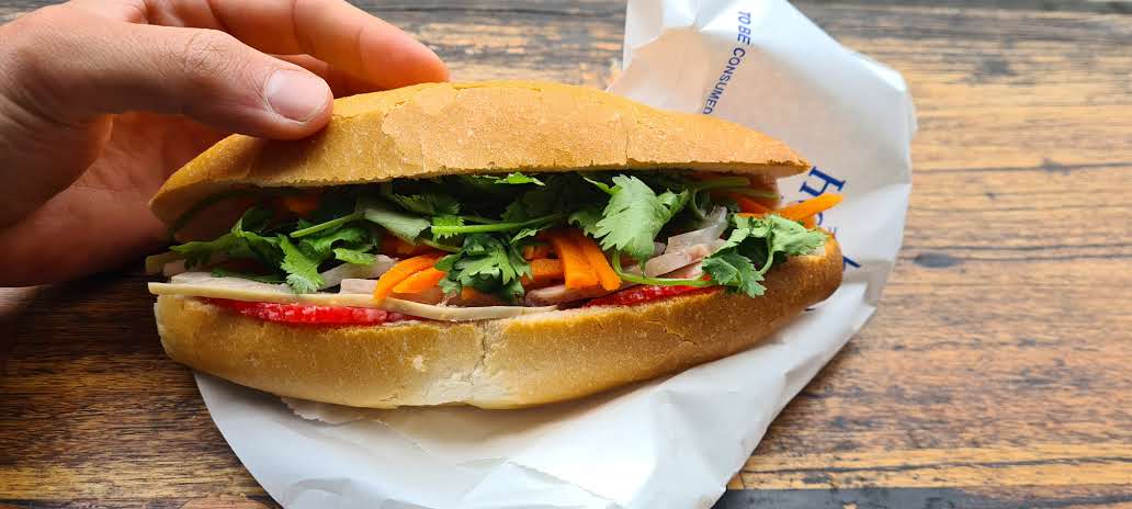 cold cut slice of pork on a bread roll with coriander and pickled carrot