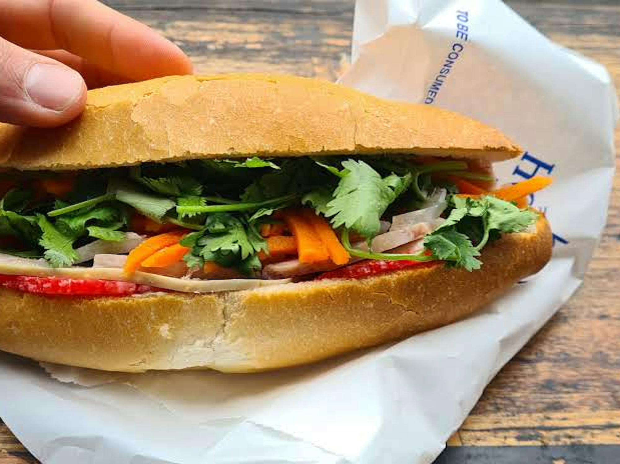 cold cut slice of pork on a bread roll with coriander and pickled carrot