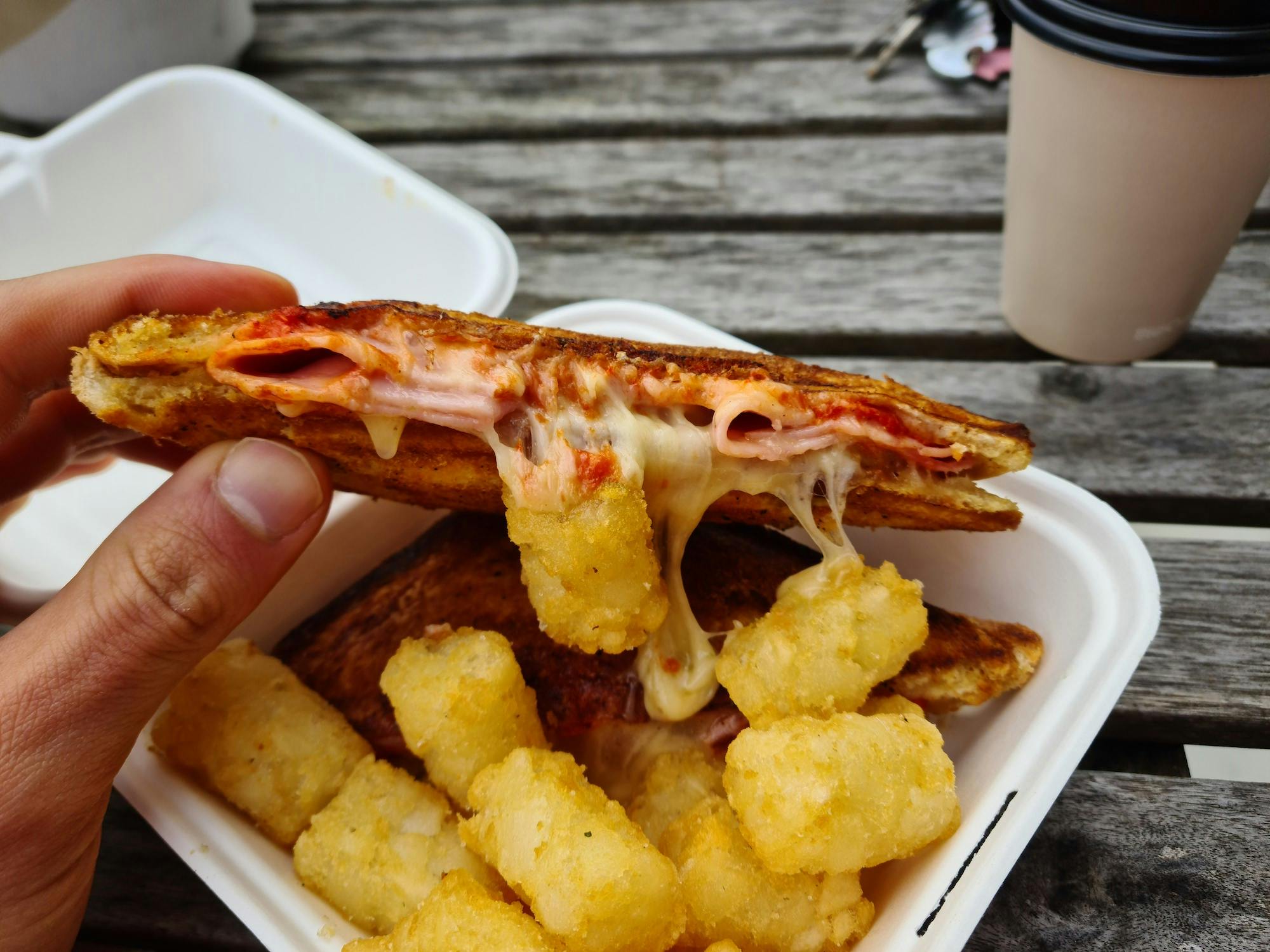 Half a jaffle held up to demonstrate the oozing cheese above a mound of potato gems.